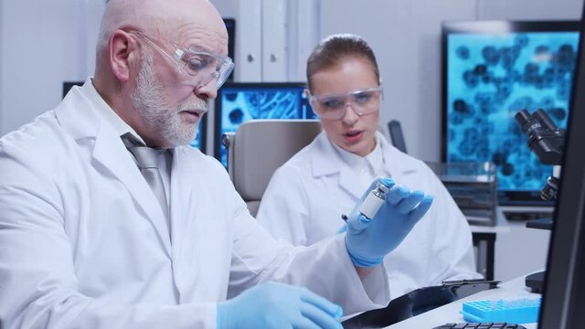 Elderly professor and young laboratory assistant are doing scientific experiment in a modern laboratory. Genetic engineers workplace. The concept of science, medicine and vaccine development.