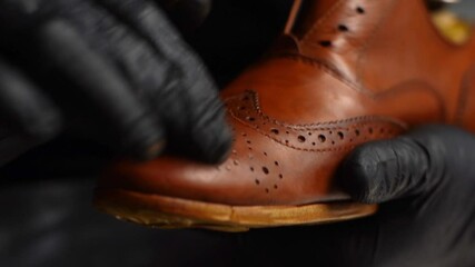 Close-up hands of unrecognizable shoemaker in black gloves rubbing paint on toe cup of light brown leather shoes with fingers. Process of repairing and restoration shoes by cobbler in shoe repair shop