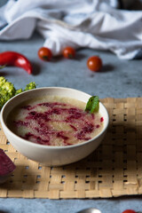 Close up of red beet and chicken soup in a bowl along with mint leaf and condiments.