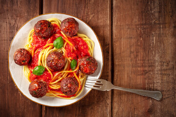 Meatballs with spaghetti and tomato sauce, shot from the top on a dark rustic wooden background with a fork and copy space