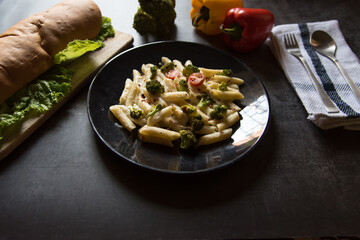 Pasta with vegetables and cheese along with bread loaf and condiments with use of selective focus.