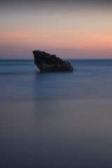 Sunset seascape. Rock in the ocean. Slow shutter speed. Soft focus. Silky water. Colorful sky. Amazing water reflection. Nature and environment background. Copy space. Beach in Bali.