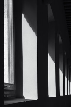 Detail of the geometry of a corridor with light entering through the windows and the shadow of the interior. Monochrome. Vertical view. © Juan
