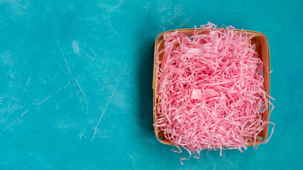 Rustic gift package. Holiday background. Organic decoration. Empty wicker basket box display with pink raffia filler for present on blue painted textured copy space.