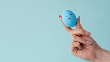 Life crisis. Conceptual banner. Trouble failure. Blue painted egg with exhausted tired dizzy face design in female hand isolated on light copy space background.