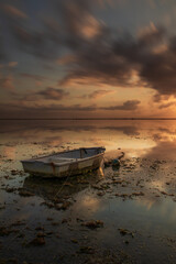 Old fisherman boat. Seascape. Fishing boat at the beach during sunrise. Low tide. Water reflection. Cloudy sky. Slow shutter speed. Soft focus. Sanur beach, Bali.