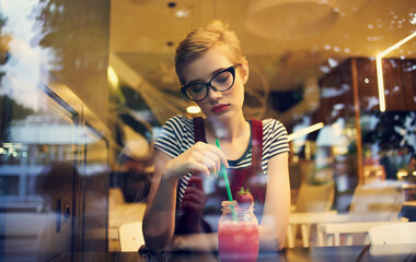 fashionable woman in red sundress sits in a cafe and mirror glass reflection of cars on the street