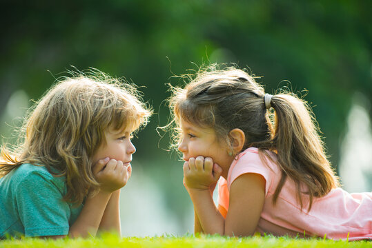Brother and sister having fun in the park, two cheerful children laying down on green grass. Happy family love and happiness concept.