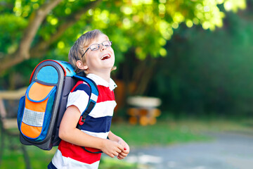 Fototapeta premium Happy little kid boy with glasses and backpack or satchel on his first day to school or nursery. Child outdoors on warm sunny day, Back to school concept.