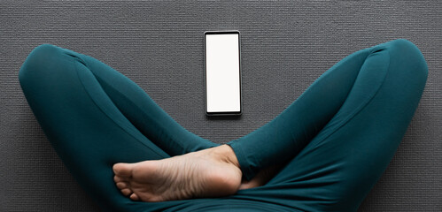 Practicing yoga at home. Online video training, smartphone with blank empty copy space mockup screen. Girl doing exercises and meditate. Meditation, relaxation, healthy lifestyle concept