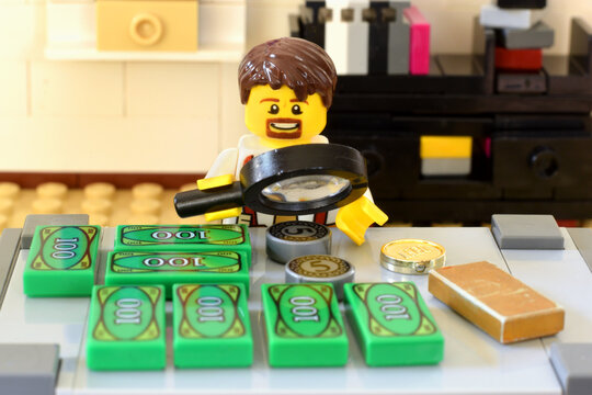 Lego minifigure in office or bank is working on the table with money cash. Editorial illustrative image of business ocuupation.