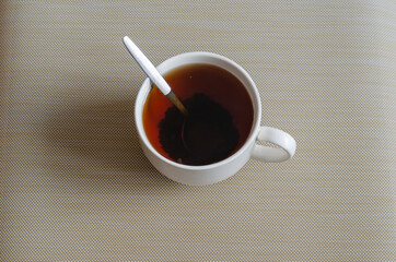 A white ceramic mug full of black tea with a metal spoon.