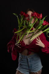 Studio portrait of a young woman on a black background with bouquet of red tulips in her hands