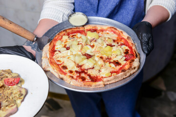 Gourmet pizza with barbeque sauce, grilled chicken, cheese served by waiter in restaurant or diner.