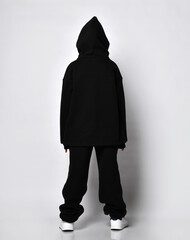 back view of a boy in a jacket with a hood and brooches on, on a light studio background