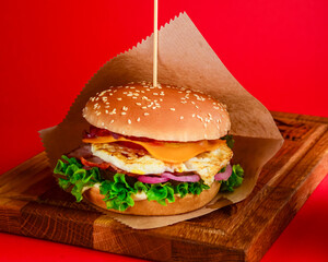 Bacon and chicken burger with red onions and cheese over red background. Fast food, junk food concept.