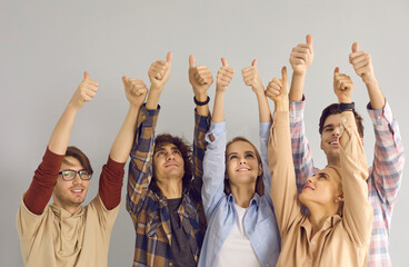 Team of happy confident young people raising hands in air, giving thumbs-up and smiling. Group of...