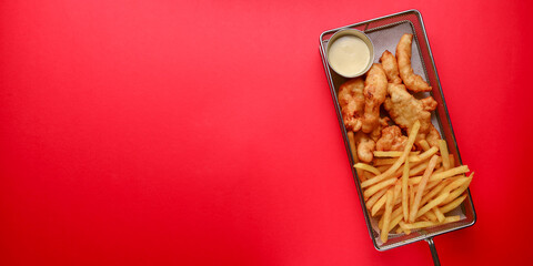 A metal tray of chicken nuggets with french fries over bright red background. Fast food, junk food concept.