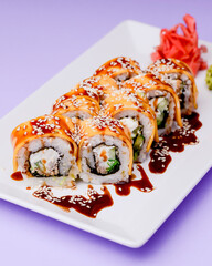 Eel, salmon and tuna sushi with unagi sauce served on a white plate over purple background.