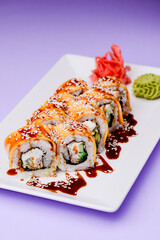 Eel, salmon and tuna sushi with unagi sauce served on a white plate over purple background.