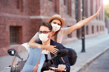 Happy mature couple wearing masks while riding a scooter in the city on a sunny day