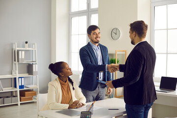 Obraz premium Caucasian man and his African-American wife receive greetings from a financial advisor with a rental home and a mortgage. Bank manager shakes hands with happy customers in the office at a meeting.