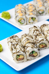 Sushi large set served on a white plate over blue background. Traditional Asian Japanese cuisine concept.