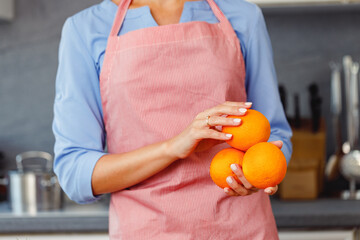 Unrecognizable woman holding oranges while standing in kitchen