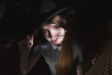 Girl in a strict gray dress and black hat with narrow brim