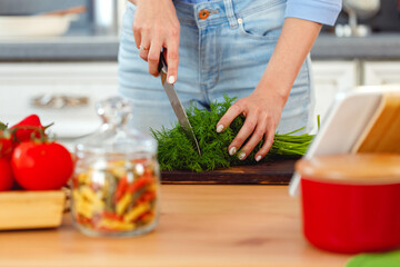 Woman cutting parsley on wooden board in kitchen
