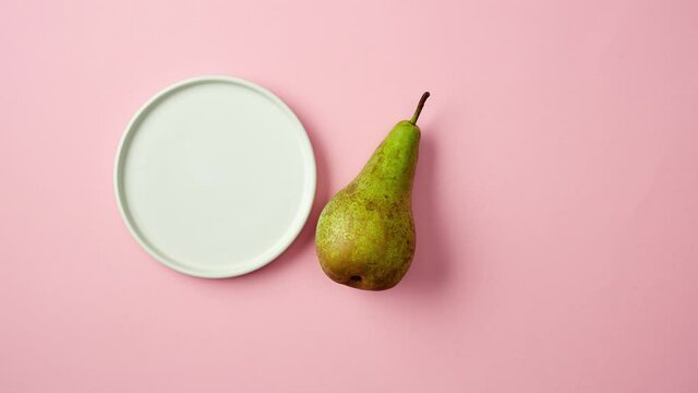 fresh ripe green pear rolls on a white plate and splits into slices. pink background, top view, stop motion animation, zoom in