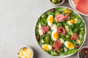 Salad with prosciutto, parmesan, olives, eggs and arugula in a plate on a gray background. Italian...