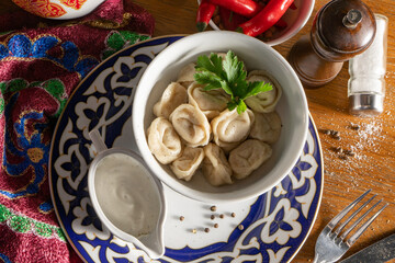 Boiled dumplings with sour cream and parsley in a plate with an Uzbek pattern