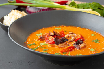 Tom Yam Thai soup in black bowl on gray table