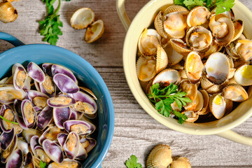 Two pots photographed from above, one blue with tellerinas and one white beige with cockles with parsley and cloves of decoration on an elegant gray rustic background