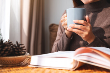 Closeup image of a woman drinking coffee while reading book at home