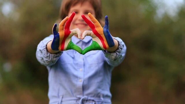 Kid hands painted in Seychelles flag color show symbol of heart and love gesture on nature background. Kid play paint hands