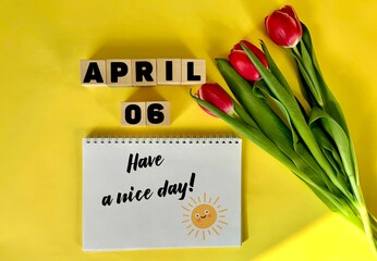 April 6 on wooden cubes on a yellow background.Next to a bouquet of tulips and a notebook with the...