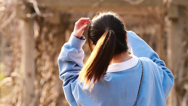 Beautiful Chinese young woman turning back with shiny black long hair and smiling pleasantly surprised in forest park, slow motion footage.