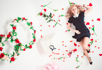 Fototapeta premium Beautiful woman in a black dress and high heels lies on a white floor with a flowers on International Women's Day.