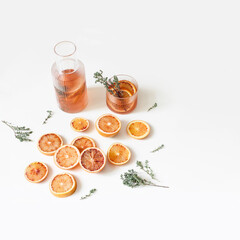 Whole and cut tangerines and blood oranges fruits. Thyme, mint herbs on wooden chopping board. White table background. Lemonade drink, cocktail in glass carafe. Food concept. Summer web banner.