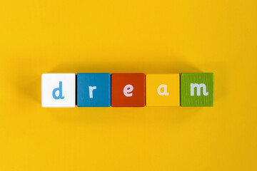 Word Dream made from colored wooden blocks. Painted cubes with letters on yellow background. Top view. Selective focus. Copy space.