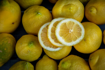 Slice of lemon along with a group of lemons on a wood table