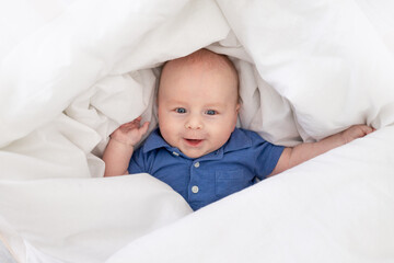smiling baby boy in a blanket in a crib, happy newborn woke up in the morning or goes to bed