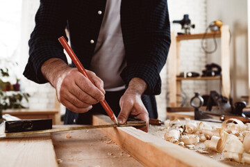Carpenter makes pencil marks on a wood plank