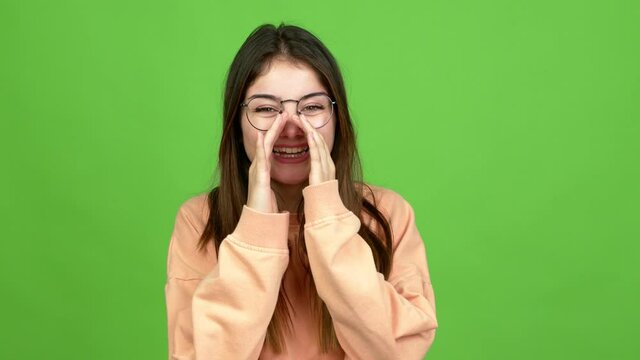 Young caucasian woman with glasses shouting and announcing something over isolated background. Green screen chroma key