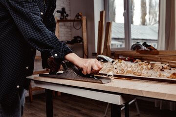 Carpenter's hands planing a plank of wood with a hand plane