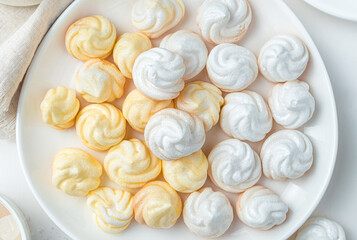Yellow and white meringues on a light background close-up. Top view, horizontal.