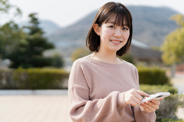 Naklejka premium 公園でスマートフォンを使う女性