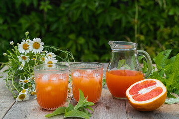 Grapefruit juice with ice cubes ,mint leaves and a bunch of daisies in the open air on a green blurred background.